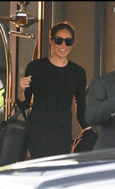 a woman in black dress and sunglasses exiting a car