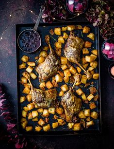 some meat and potatoes on a tray next to glasses of wine, candles and flowers