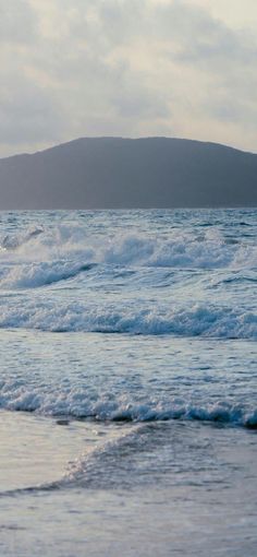 a person riding a surfboard on top of a wave in the ocean with mountains in the background