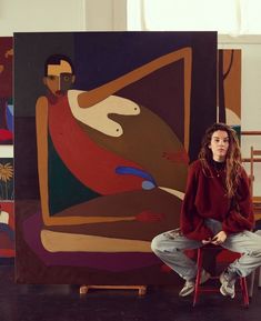 a woman sitting on a chair in front of some art work and posing for the camera