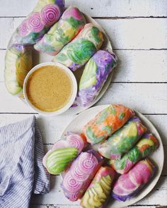 two plates filled with colorfully decorated rolls next to a bowl of dipping sauce