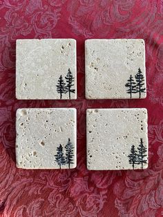 four coasters with black trees on them sitting on a red tablecloth covered surface