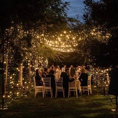 a group of people sitting around a dinner table covered in fairy lights at night time