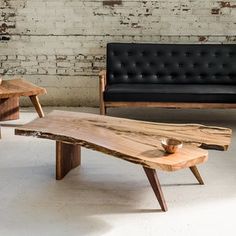 two wooden tables sitting next to each other in front of a black leather couch and white brick wall