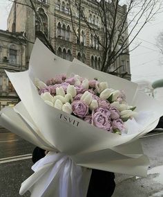 a woman holding a bouquet of flowers on the street in front of an old building