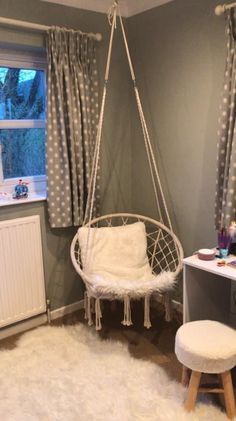 a bedroom with a hanging chair, desk and window in the corner that has polka dot curtains on it