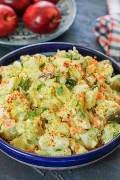 a blue bowl filled with potato salad next to apples