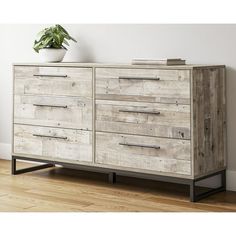 a white dresser sitting on top of a wooden floor next to a potted plant