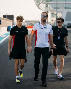 three men walking down a race track wearing black and white shirts with red trims