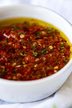 a white bowl filled with marinara sauce on top of a cloth covered tablecloth