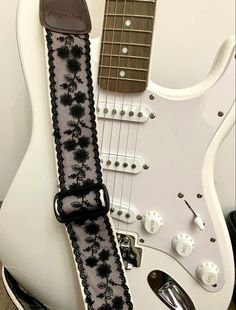 an electric guitar strap with black flowers on it, sitting in front of a white guitar