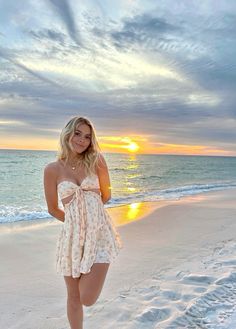 a woman standing on top of a sandy beach next to the ocean at sun set