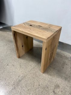 a small wooden bench sitting on top of a cement floor next to a white wall