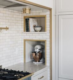 a kitchen with white brick walls and gold trim on the hood, stove top and cabinets