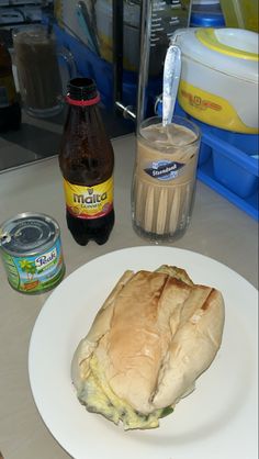 a sandwich sitting on top of a white plate next to a bottle of soda and an ice cream container