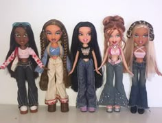 five dolls standing next to each other in front of a white wall and one has her hair pulled back