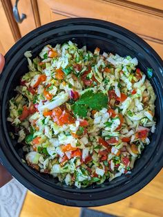 a person holding a black bowl filled with coleslaw