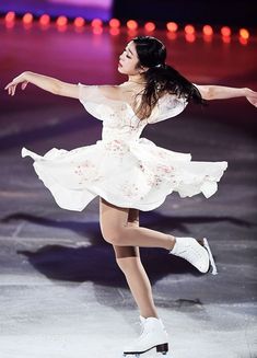 a female figure skating on the ice in a white dress and white tennis shoes with her arms outstretched