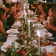 a group of people sitting at a table with plates and candles on it in front of them