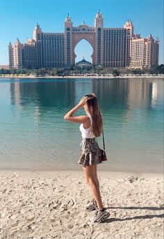 a woman standing on top of a sandy beach next to a large body of water