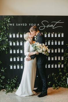 a bride and groom kissing in front of a black backdrop that says we saved you a seat