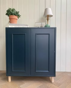 a blue cabinet sitting on top of a wooden floor next to a lamp and potted plant