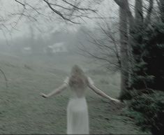 a woman in a white dress is walking through the woods with her arms spread out