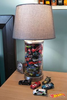 a lamp that is on top of a table with toy cars in the jar underneath it