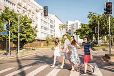 three girls crossing the street in front of a red traffic light and two men walking behind them