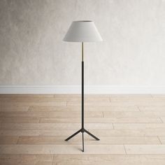 a floor lamp with a white shade on it in an empty room next to a wall