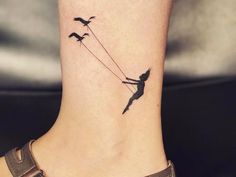 a small tattoo on the ankle of a girl with birds flying behind her and holding onto a string