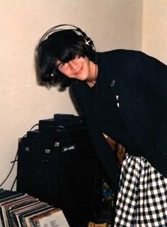 a young man wearing headphones standing next to a stack of records