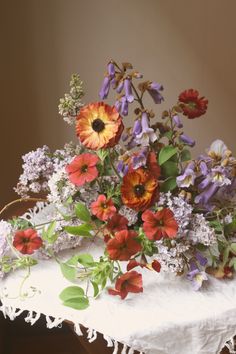 a bunch of flowers that are sitting on a white table cloth and some plants in the background