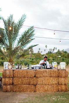 a man sitting at a table covered in hay next to a palm tree on top of a field