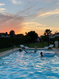 a swimming pool with lounge chairs and people in the water at sunset or sunrise time