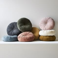 four different colored round cushions sitting on top of a white shelf next to each other