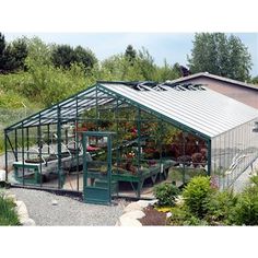 a green house sitting in the middle of a garden filled with lots of plants and flowers