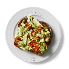 an open face sandwich topped with avocado and other toppings on a white plate