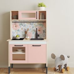 a wooden toy kitchen with pink cabinets and flowers on the wall behind it is an elephant figurine