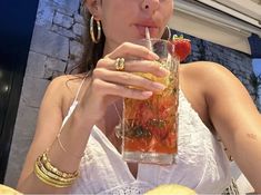 a woman drinking from a tall glass with strawberries in it and holding a straw