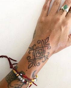 a woman's hand with tattoos and bracelets on her wrist, next to a white wall