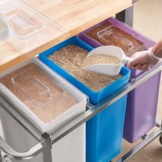 a person scooping cereal into three bins on a metal cart with plastic containers