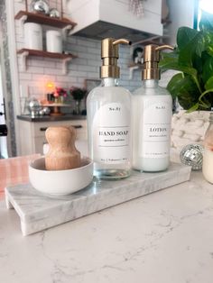 two soap dispensers sit on a marble countertop next to a potted plant