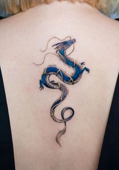 a woman's back with a blue and gold dragon tattoo on her left shoulder