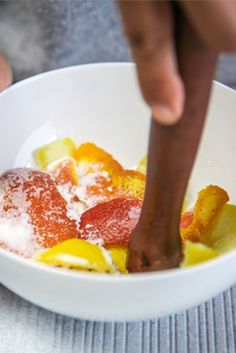 a white bowl filled with fruit covered in powdered sugar and a wooden spoon sticking out of it