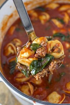 a ladle full of pasta and spinach soup being held up by a spoon