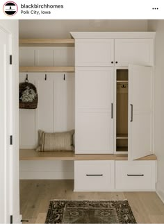 a white closet with wooden shelves and drawers next to a rug on the floor in front of it