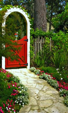 a red door in the middle of a garden with pink and white flowers around it