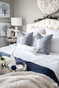 a white bed topped with pillows and blankets next to a night stand filled with flowers