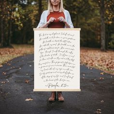 a woman holding up a sign with writing on it in front of trees and leaves